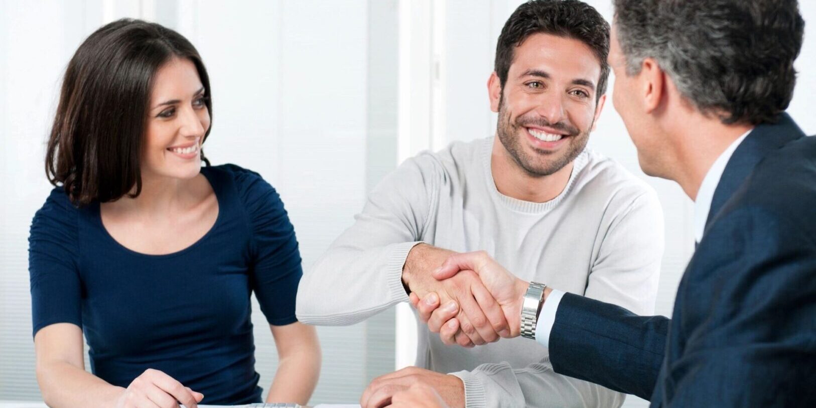 A man and woman shaking hands over a table.