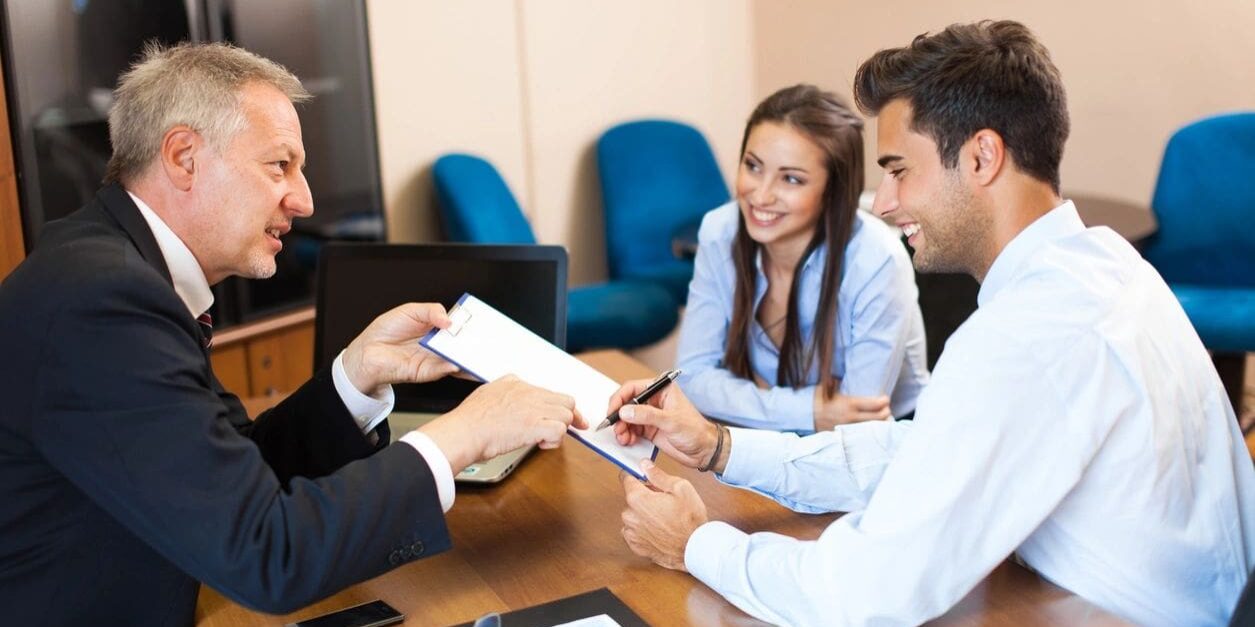 A man handing over paperwork to two people.